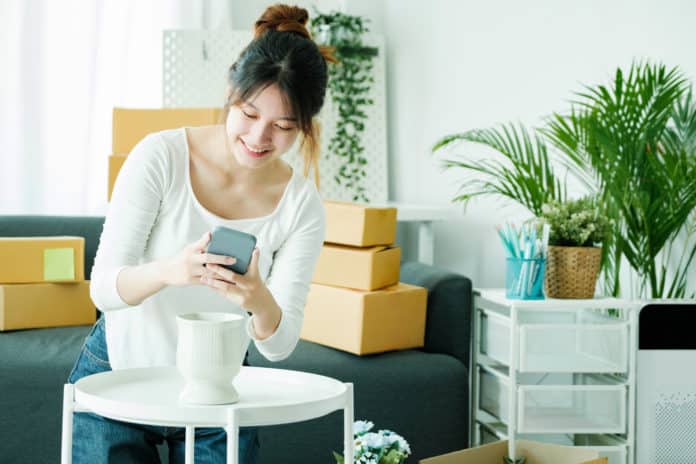 Young asian business owner holding phone and retail package parcel.